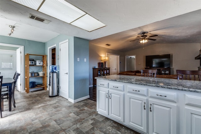 kitchen with baseboards, visible vents, white cabinets, a ceiling fan, and vaulted ceiling