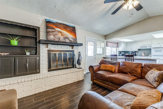 living room featuring lofted ceiling, wood finish floors, a brick fireplace, and a ceiling fan