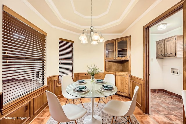 dining room featuring a chandelier, a tray ceiling, a wainscoted wall, and crown molding