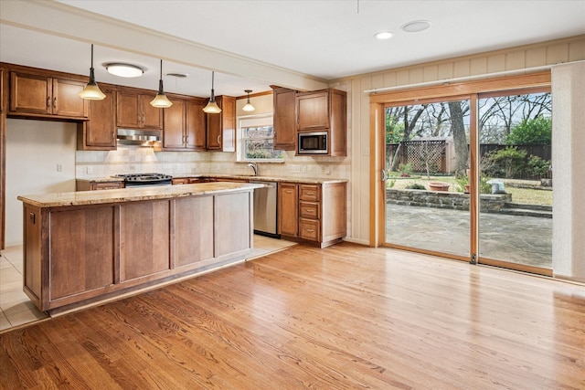 kitchen featuring a wealth of natural light, stainless steel appliances, under cabinet range hood, and light stone countertops