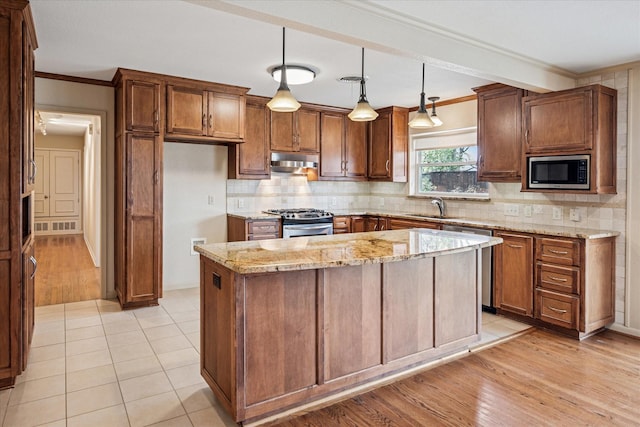 kitchen featuring light stone countertops, a sink, stainless steel appliances, under cabinet range hood, and tasteful backsplash