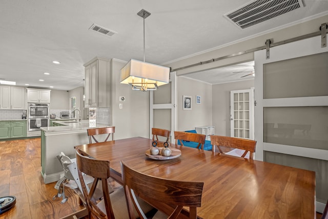 dining area with light wood-type flooring, visible vents, a barn door, and ornamental molding