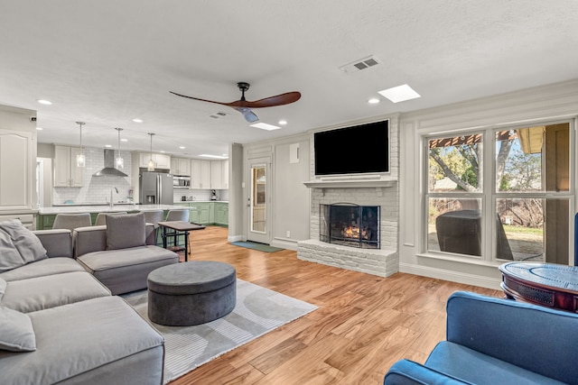 living area featuring light wood-type flooring, visible vents, a brick fireplace, and recessed lighting