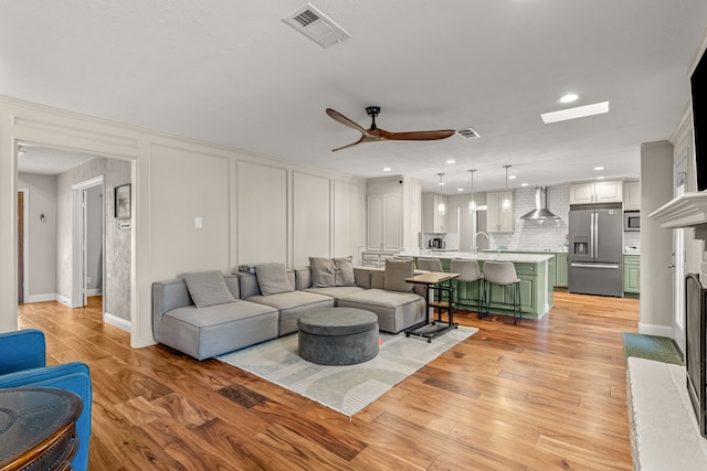 living area with visible vents, light wood finished floors, ceiling fan, and a decorative wall