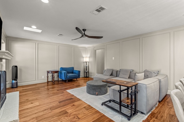 living area featuring a decorative wall, ceiling fan, light wood-style flooring, and visible vents