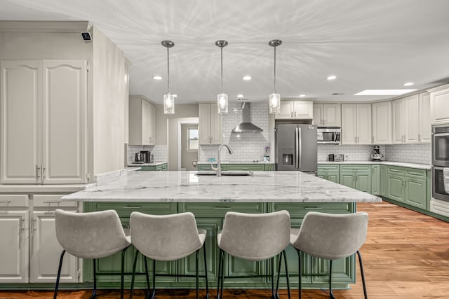 kitchen with a kitchen bar, light wood-type flooring, appliances with stainless steel finishes, wall chimney exhaust hood, and a sink