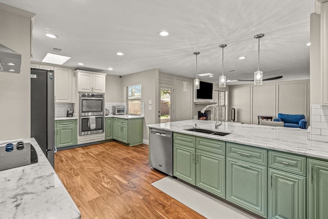 kitchen featuring a sink, white cabinets, light wood-style floors, appliances with stainless steel finishes, and green cabinets