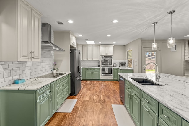 kitchen with a sink, white cabinetry, appliances with stainless steel finishes, green cabinets, and wall chimney exhaust hood