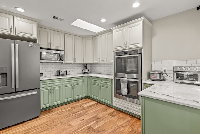 kitchen with white cabinets, light wood-type flooring, green cabinetry, and stainless steel appliances