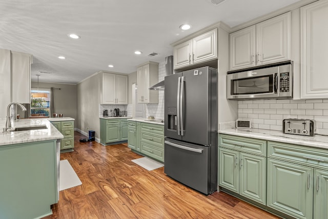 kitchen with wood finished floors, green cabinetry, a sink, stainless steel appliances, and wall chimney exhaust hood