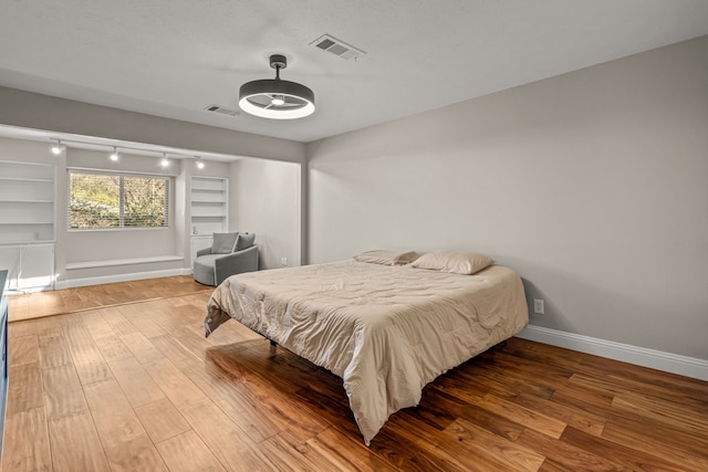 bedroom with visible vents, wood finished floors, baseboards, and track lighting