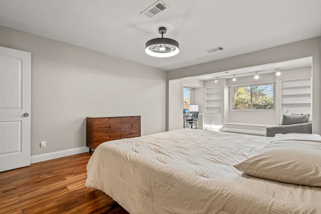 bedroom with visible vents, baseboards, wood finished floors, and rail lighting