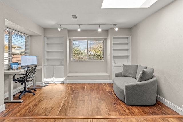 home office featuring built in features, wood finished floors, visible vents, baseboards, and a skylight