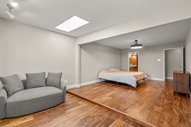 bedroom with ensuite bathroom, baseboards, and wood finished floors