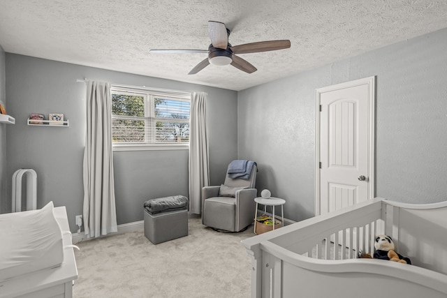 carpeted bedroom with a crib, a textured ceiling, baseboards, ceiling fan, and a textured wall