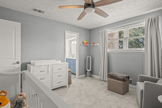 bedroom with a ceiling fan, visible vents, a crib, a textured ceiling, and light carpet