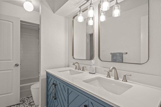 bathroom with double vanity, toilet, a textured wall, and a sink