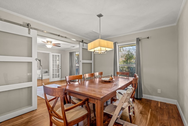 dining area with a barn door, wood finished floors, french doors, and ornamental molding