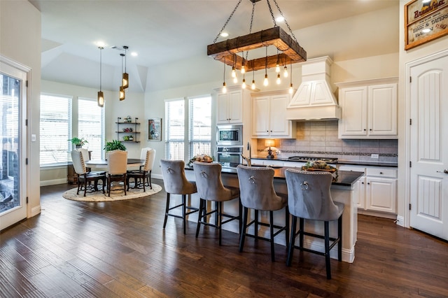 kitchen with a breakfast bar area, dark countertops, decorative backsplash, appliances with stainless steel finishes, and premium range hood