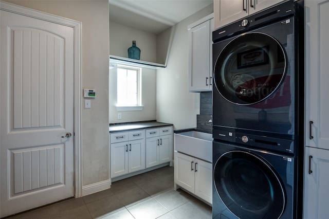 laundry room featuring light tile patterned floors, cabinet space, a sink, and stacked washer and clothes dryer