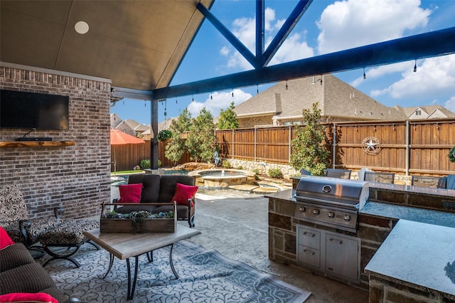 view of patio / terrace with area for grilling, a fenced backyard, an in ground hot tub, exterior kitchen, and a fireplace