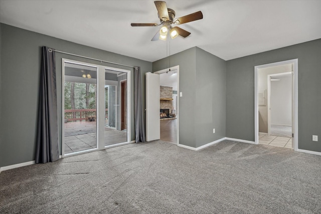 carpeted empty room with ceiling fan, a lit fireplace, and baseboards