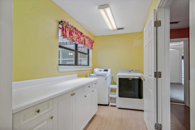 laundry area featuring cabinet space, washing machine and dryer, a textured ceiling, and light wood-style floors