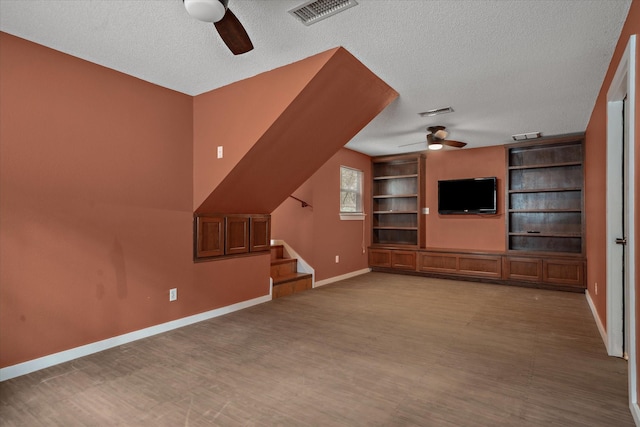 unfurnished living room featuring a textured ceiling, visible vents, baseboards, stairs, and a ceiling fan