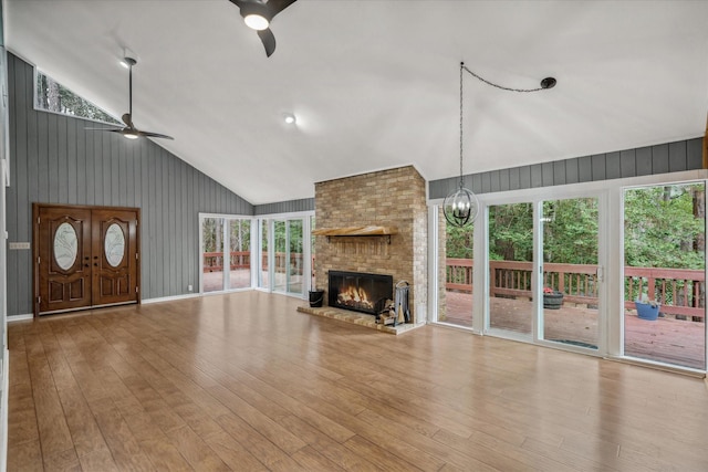 unfurnished living room with a brick fireplace, high vaulted ceiling, wood finished floors, and ceiling fan with notable chandelier