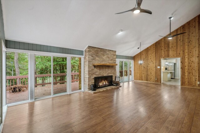 unfurnished living room featuring wood walls, ceiling fan, a fireplace, and wood finished floors