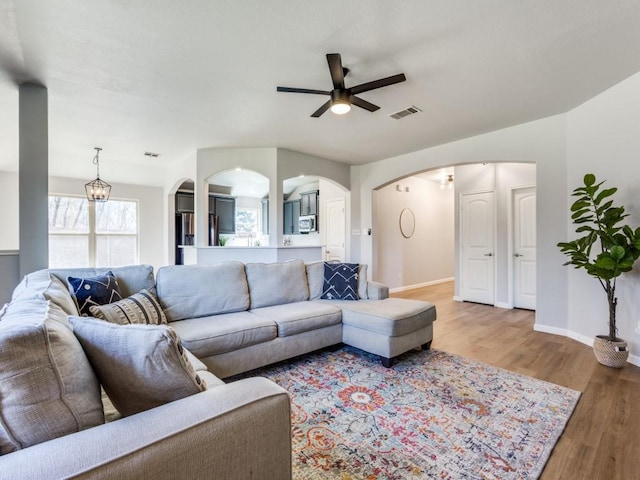 living room with arched walkways, visible vents, a ceiling fan, wood finished floors, and baseboards