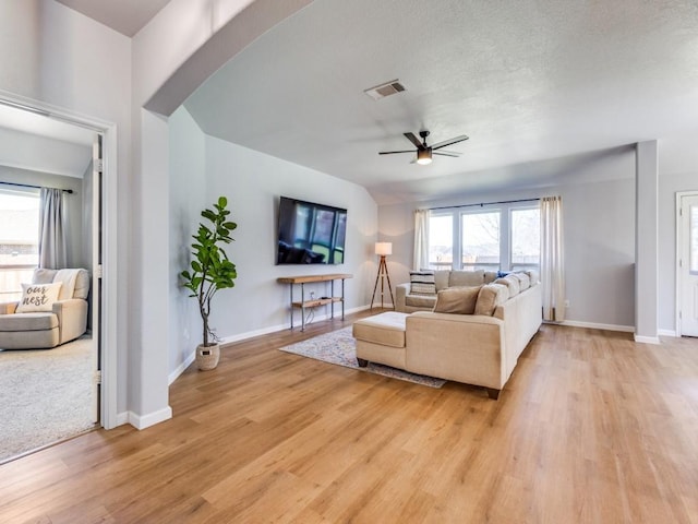 living area featuring visible vents, light wood-style flooring, ceiling fan, a textured ceiling, and baseboards