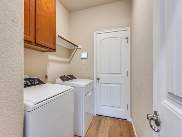 washroom with cabinet space, light wood finished floors, and washing machine and clothes dryer