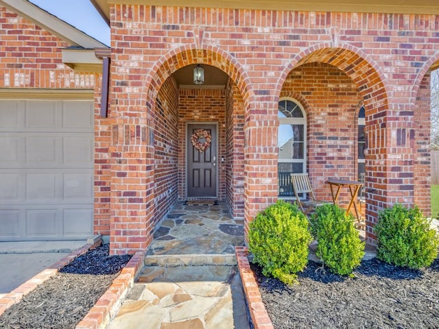 view of exterior entry with an attached garage and brick siding