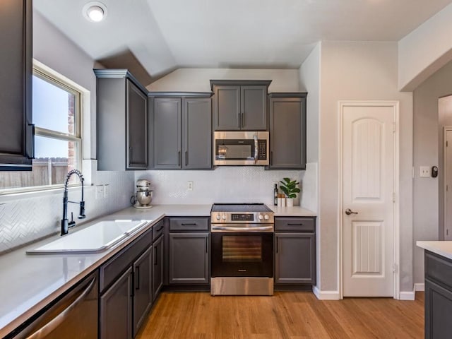 kitchen with light wood finished floors, decorative backsplash, appliances with stainless steel finishes, light countertops, and a sink