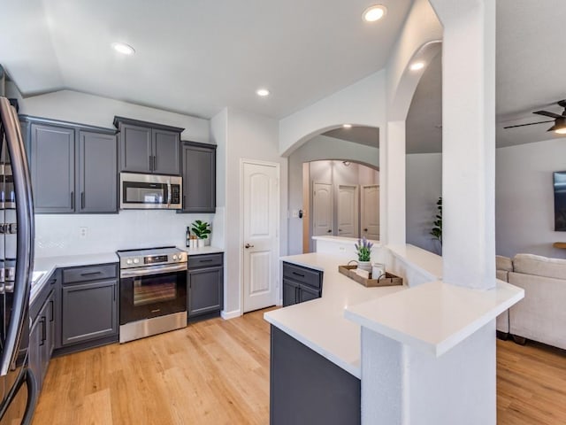 kitchen featuring appliances with stainless steel finishes, open floor plan, light countertops, light wood-type flooring, and backsplash