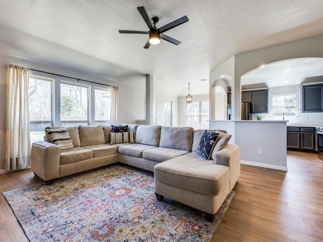 living area with a textured ceiling, a ceiling fan, arched walkways, and wood finished floors