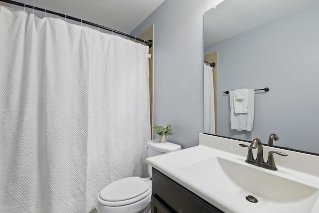 full bath featuring toilet, a textured wall, and vanity