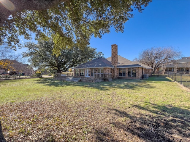 rear view of property with a lawn, a fenced backyard, a chimney, a deck, and central AC