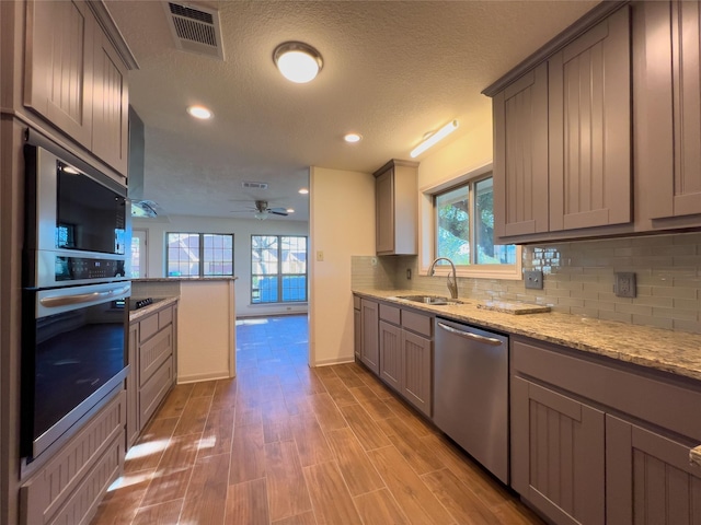 kitchen with gray cabinetry, a sink, visible vents, stainless steel dishwasher, and backsplash