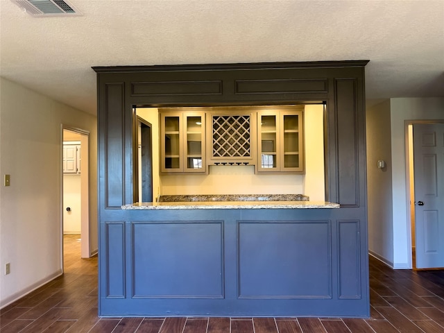 bar with a textured ceiling, wood finish floors, visible vents, baseboards, and a dry bar