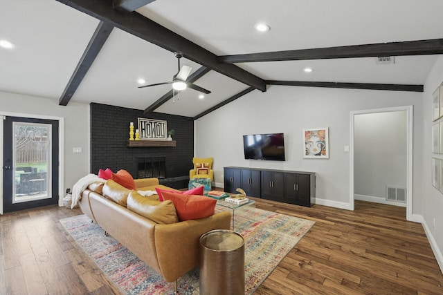 living room with visible vents, baseboards, lofted ceiling with beams, wood finished floors, and a fireplace