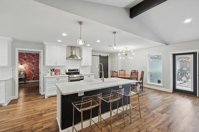 kitchen featuring backsplash, a barn door, stainless steel range with electric cooktop, a sink, and wall chimney range hood