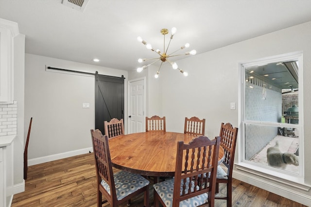 dining room with a barn door, baseboards, visible vents, wood finished floors, and an inviting chandelier