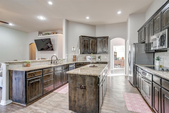 kitchen featuring arched walkways, a center island, stainless steel appliances, a sink, and a peninsula