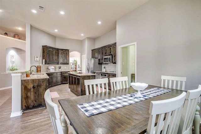 dining space with arched walkways, light wood-style flooring, recessed lighting, visible vents, and baseboards