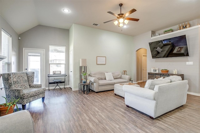 living room featuring baseboards, arched walkways, a ceiling fan, lofted ceiling, and light wood-style floors