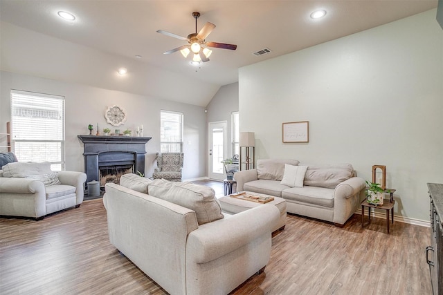 living area featuring vaulted ceiling, a fireplace, visible vents, and light wood-style floors