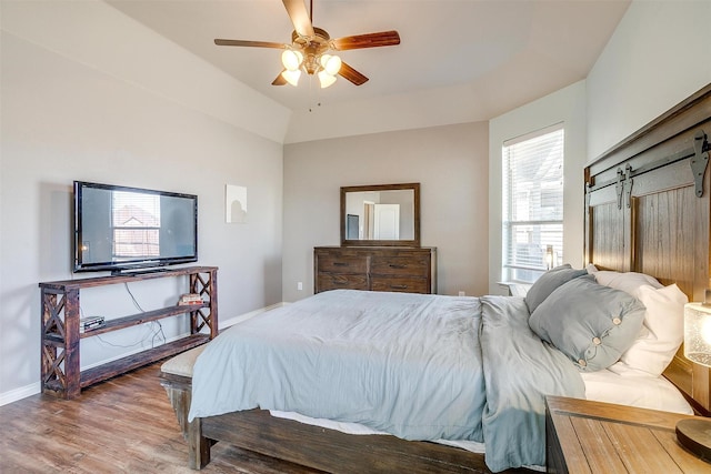 bedroom with ceiling fan, a barn door, wood finished floors, and baseboards