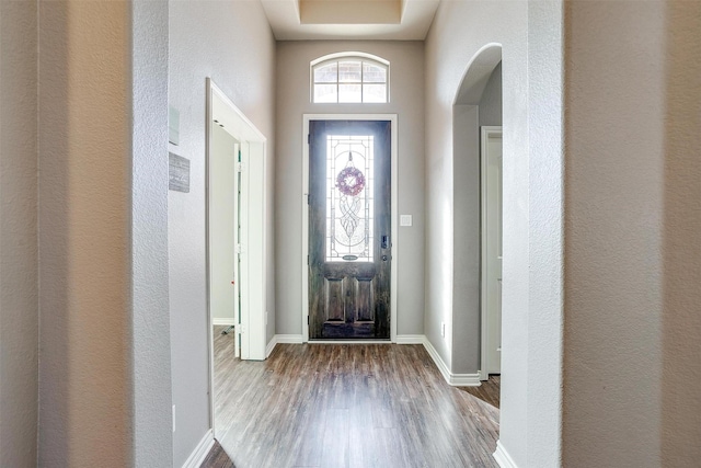 entrance foyer with baseboards, arched walkways, wood finished floors, and a textured wall